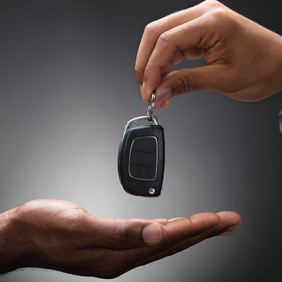 Close-up Of Hand Handing Car Key To The Person Against Gray Background